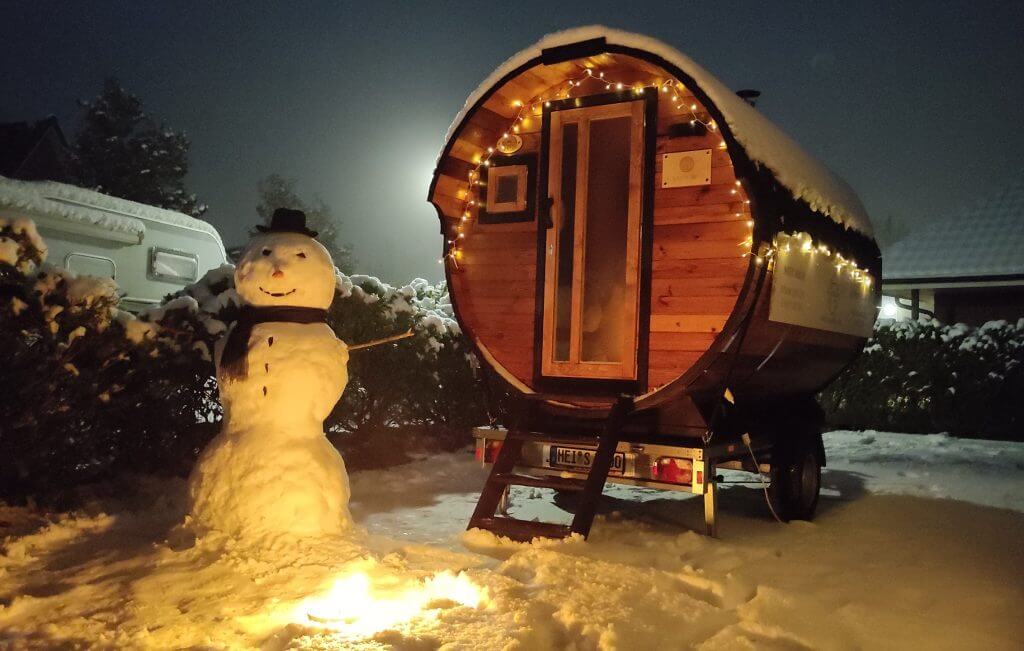 Fasssauna im Schnee mit Schneemann und Lichterkette
